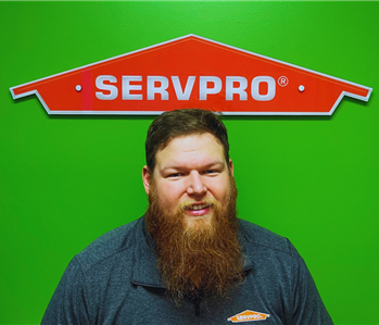 male employee in black smiling in front of green wall with orange servpro house